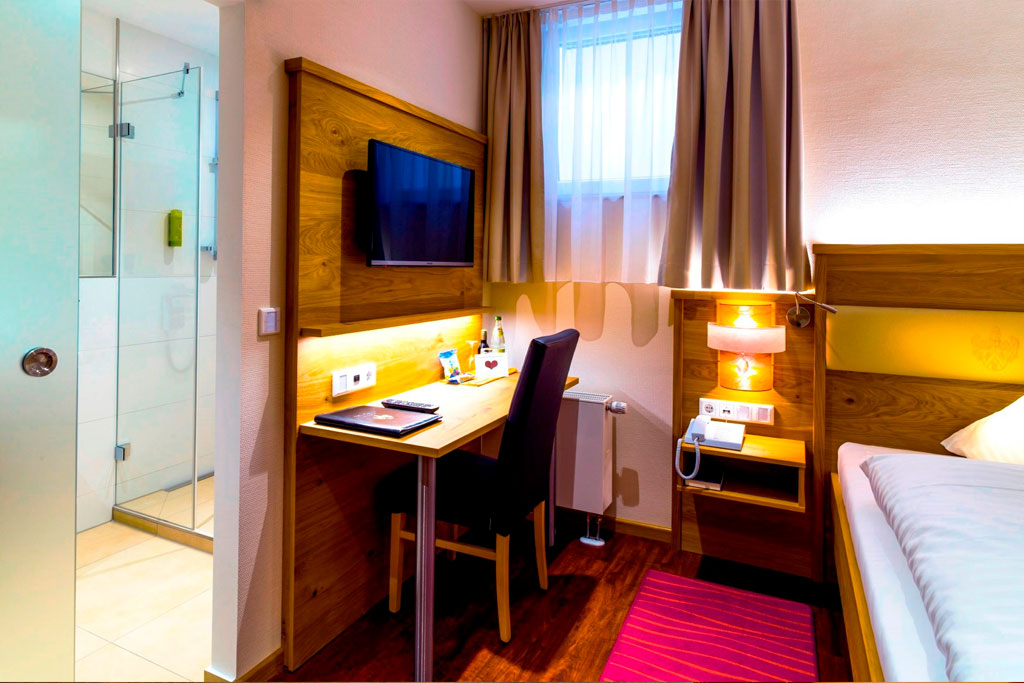 Hotel Asemann Planegg Single Room in the Basement A cosy single room in the basement of the Hotel Asemann in Planegg, featuring a wooden single bed, a desk, a large wall mirror and a carpet runner.
