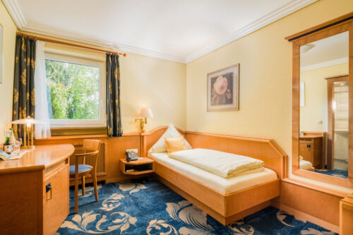 Gemütliches Einzelzimmer im Hotel Asemann in Planegg mit Holzmöbeln, Schreibtisch und Blick ins Grüne – ideal für Geschäftsreisende.