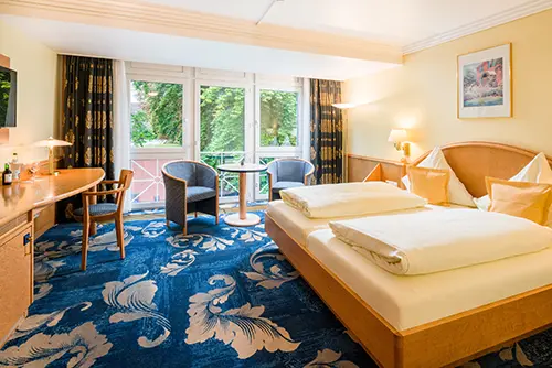 Helles und geräumiges Comfort-Doppelzimmer im Hotel Asemann in Planegg mit großem Doppelbett, gemütlicher Sitzecke und bodentiefen Fenstern zum Garten.