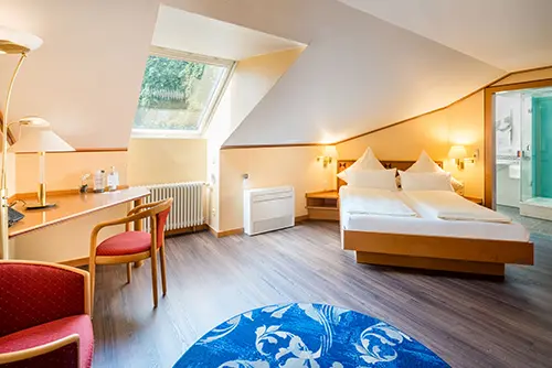 Helles Doppelzimmer im Dachgeschoss des Hotel Asemann in Planegg mit gemütlichen Dachschrägen, großem Doppelbett, Schreibtisch und modernem Bad.