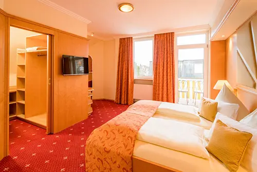 Großzügiges Doppelzimmer in der Turmvilla des Hotel Asemann in Planegg mit Doppelbett, begehbarem Kleiderschrank und eigenem Balkon.